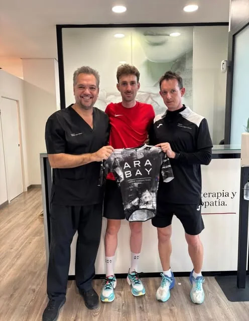 Un ciclista con su maillot junto a Antonio y otro fisioterapeuta en la recepción